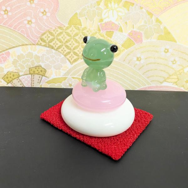 鏡餅（カエル乗せ）ちりめん台付のガラス細工の置物です。【大きさ】約高さ３２ミリ　　横幅３０ミリ　　　　　奥行３０ミリ＊商品は一つ一つ手造りのため大きさや色合いなどが写真と異なる場合がありますのでご了承をお願い致します。