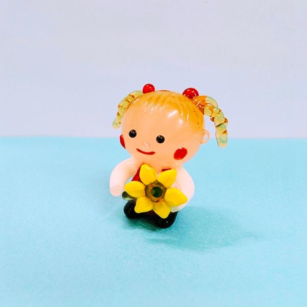 女の子とひまわりのガラス細工の置物です。【大きさ】約高さ２５ミリ　　横幅２５ミリ　　　　　奥行１８ミリ＊商品は一つ一つ手造りのため大きさや色合いなどが写真と異なる場合がありますのでご了承をお願い致します。