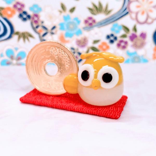 ご縁ふくろうイエローのガラス細工の置物です。＊5円は本物を磨いてます。布はちりめん素材です。【大きさ】約高さ２２ミリ　　横幅４０ミリ　　　　　奥行２０ミリ　　　布台４０ｘ２０ミリ＊商品は一つ一つ手造りのため大きさや色合いが写真と異なる場合が...