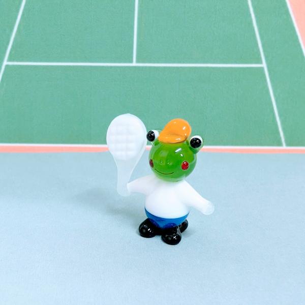 カエルのテニスのガラス細工の置物です。【大きさ】約高さ２８ミリ　　横幅２５ミリ　　　　　奥行１２ミリ＊商品は一つ一つ手造りのため大きさや色合いなどが写真と異なる場合がありますのでご了承をお願い致します。