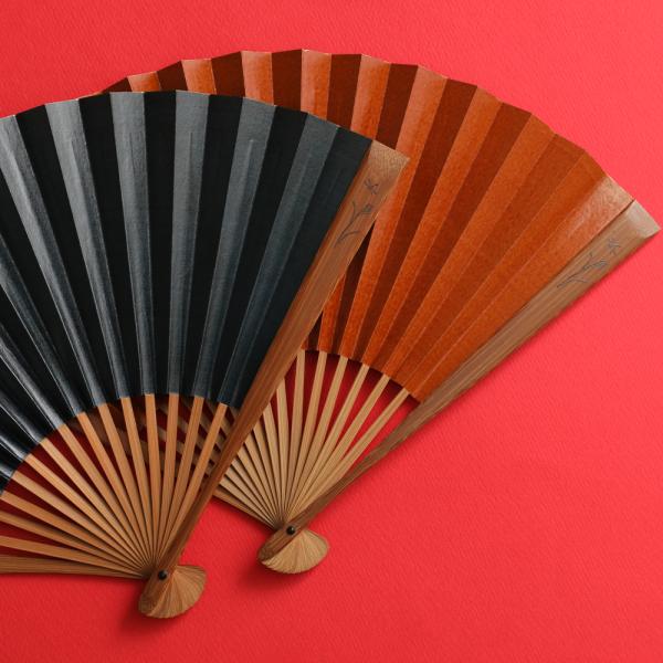 扇面に柿渋を塗った茶色と紺色の渋扇です。渋柿から搾り取った柿渋を重ね塗ることで独特のツヤと紙の強度が高められます。近年では抗菌作用を持つ天然成分として注目を浴びています。職人が一枚いちまい刷毛で色引き・柿渋引きをしております。目を凝らすと刷...
