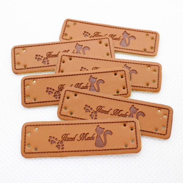 猫と肉球のシルエット、HANDMADEの文字が入った革タグ3枚セット。他の種類も販売中です。※今回のロットは、ホールの素材が残っているものが含まれます。穴は貫通しており、針も通ります。（画像5枚目にてご確認ください）◆サイズ:約15mm×5...
