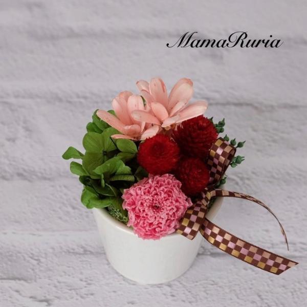 白い陶器の器に、レッド＆ピンク系のお花をアレンジしました。見る人に元気を与えるアレンジメントです！母の日やお誕生日、さまざまなお祝いの贈り物にいかがでしょうか？簡易ラッピングにてお届けします。●サイズアレンジの大きさ　直径約9センチ　高さ約...