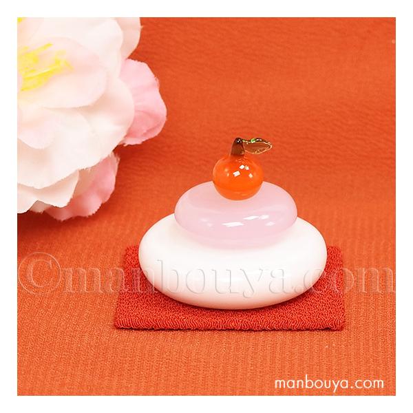 小さい硝子製のかがみ餅。ちりめんの赤い台と、みかんがセットになっています。みかんは接着されていないので他のものを乗せることもできます。かわいい白とピンクのお餅で、お正月だけでなく雛祭りの飾りにも良さそうです。【サイズ】鏡餅：約直径3×高さ1...